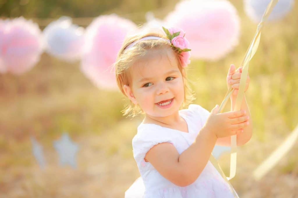 Toddler girl celebrates birthday outside with tissue paper pom poms on a string in the background