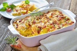 Cheesy, potato gratin dish served in ceramic pan with a plate of food in the background