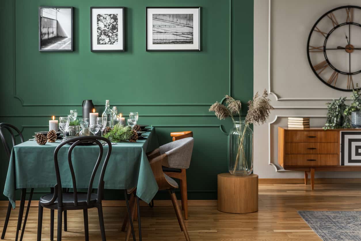 Dark green dining room matching 2023 paint trend with natural elements, black chairs, airy plants