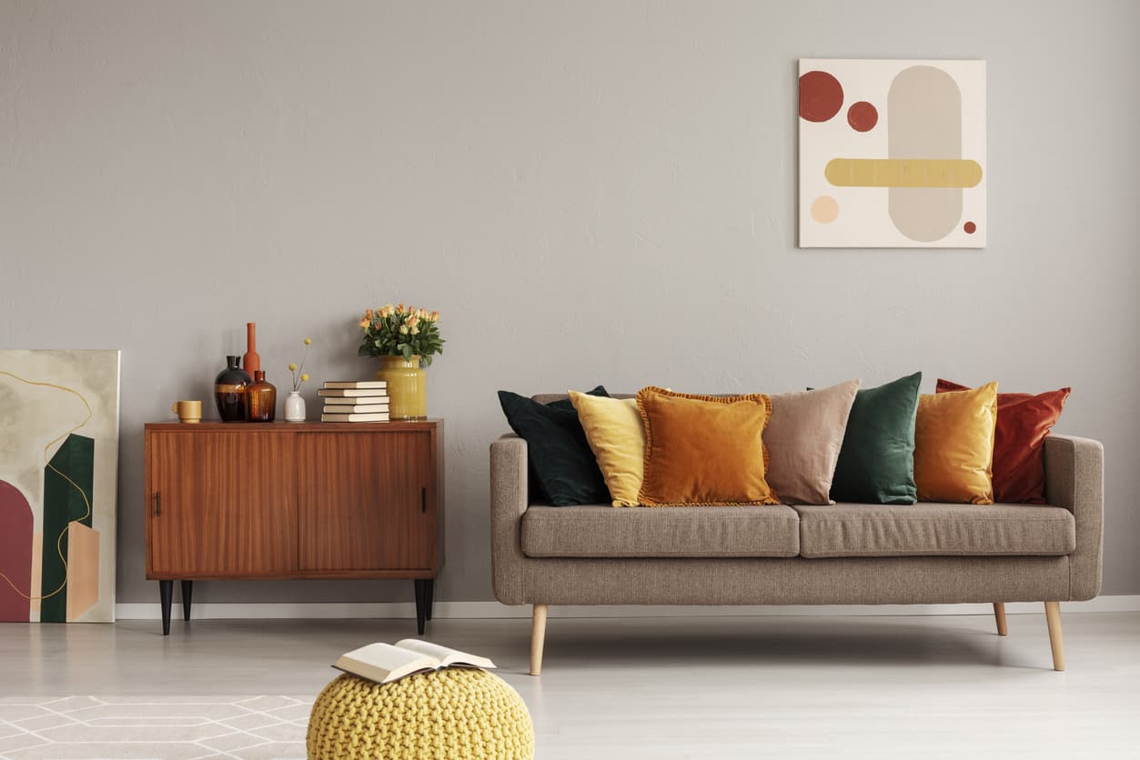 Greige living room with 2023 paint trend and retro pops of orange and yellow pillows