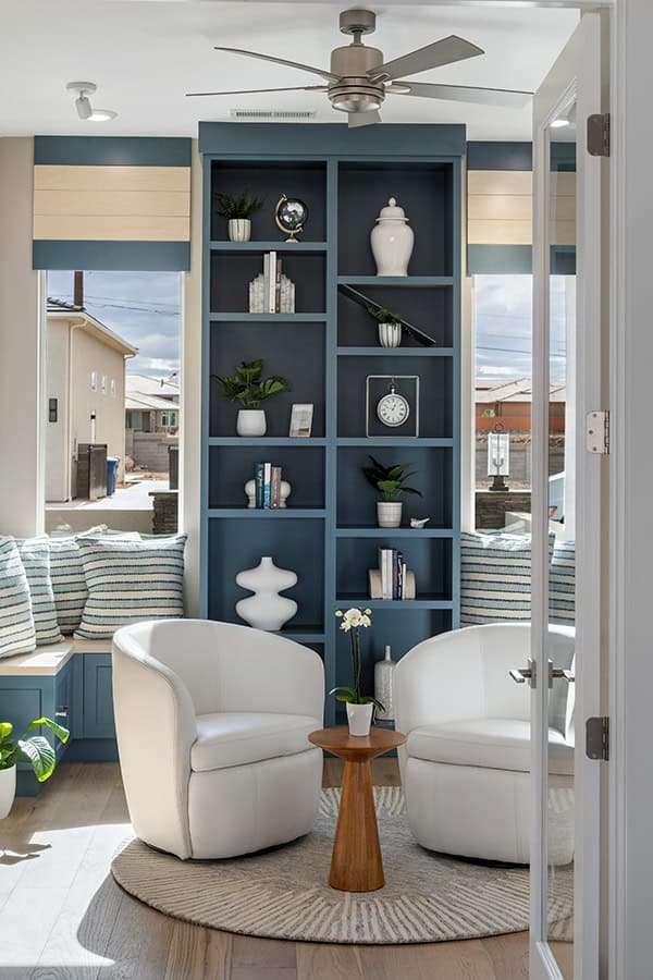 Peeking in to living room with central well-decorated book shelf in warm blue with two white accent chairs in front